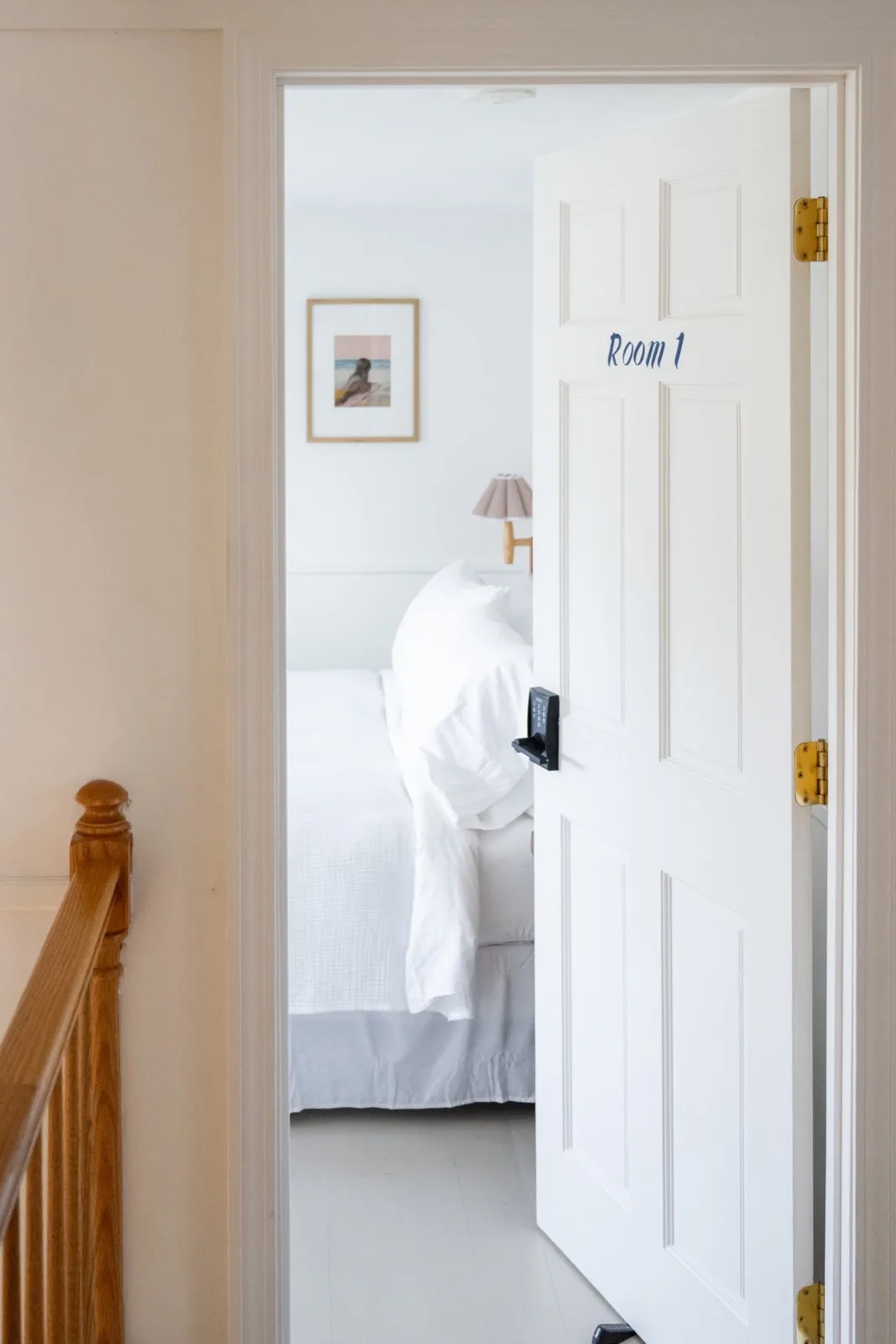 Room 1 doorway at the North Haven Inn: white linens, warm light, brass hardware